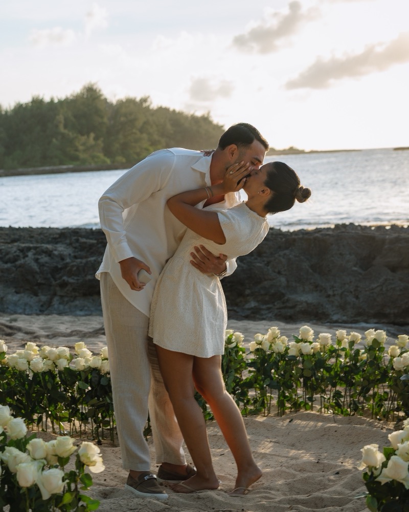 A couple kisses inside a circle of white roses after their beach proposal at Turtle Bay on Oahu