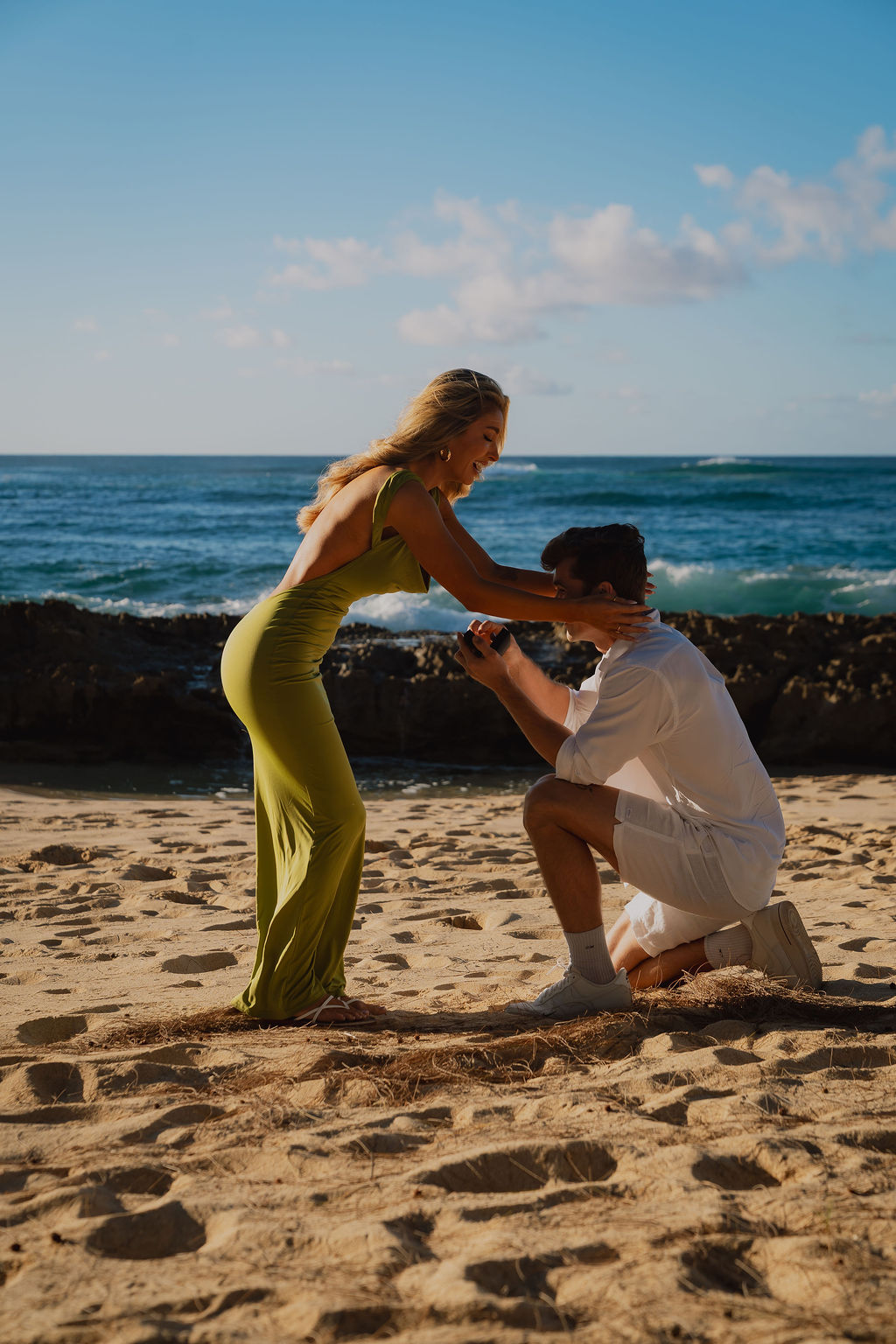 Surprise beach proposal at Turtle Bay, Oahu: he kneels with the ring as she reacts, planned and photographed by Experience Aloha Co